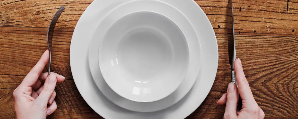 Person looking at empty plate during intermittent fasting challenges and potential downsides